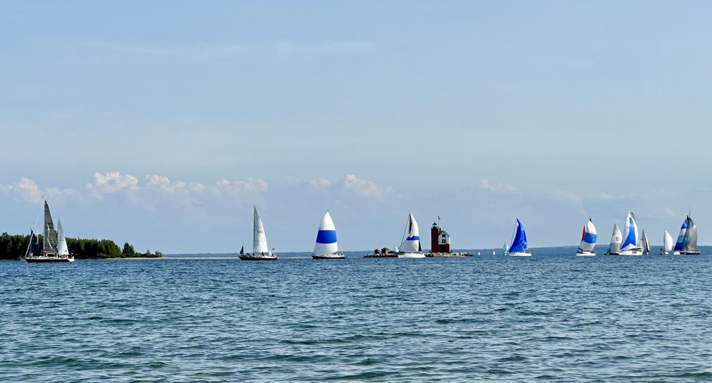 Several sailboats under spinnaker sailing new the Round Island Lighthouse.